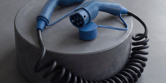 Black coiled EV charging cable with blue Type 2 ends arranged on concrete